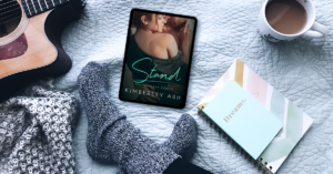 Cover of Stand surrounded by a pair of feet in thick gray socks, notebooks, a cup of coffee, a guitar and a black and white scarf.