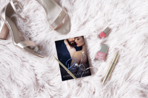 Cover of Rise lying on a thick shaggy coverlet, surrounded by a pair of silver sandals, a lipstick, nail polish and a fancy pen.